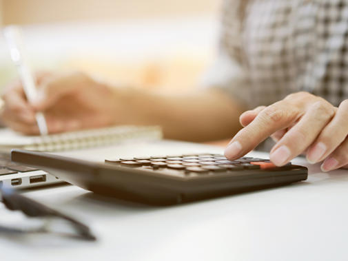 Detail of a woman's hand using a calculator and holding a pen in her other hand.